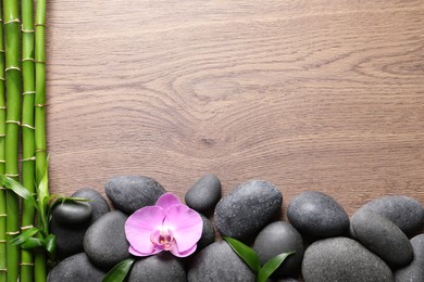 Spa stones, beautiful orchid flower and bamboo stems on wooden table, flat lay. Space for text