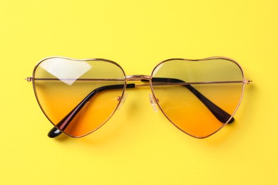 Stylish elegant heart shaped sunglasses on yellow background, top view