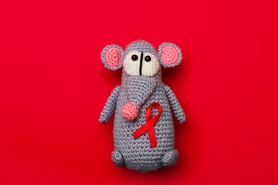 Cute knitted toy mouse with ribbon on red background, top view. AIDS disease awareness