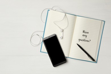 Notebook with phrase HAVE ANY QUESTIONS and smartphone on white wooden table, flat lay