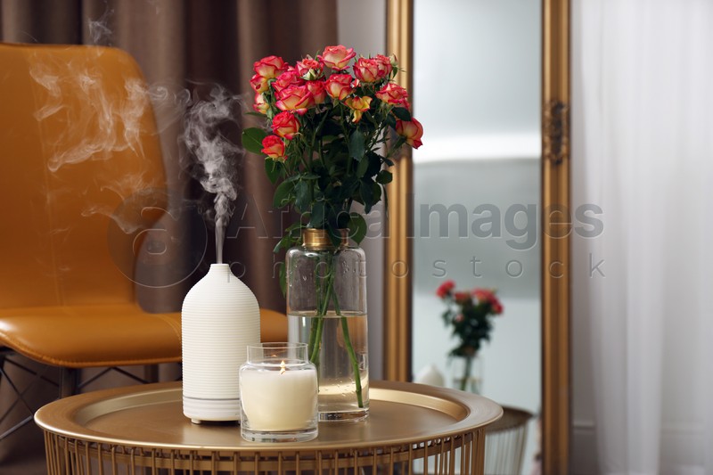 Aroma oil diffuser, burning candle and beautiful roses on table indoors, space for text. Interior elements