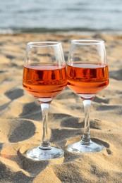 Photo of Glasses of tasty rose wine on sand near sea