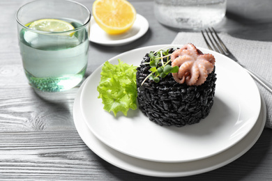 Photo of Delicious black risotto with baby octopus on grey wooden table