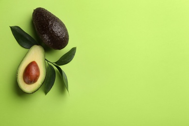 Ripe avocadoes and leaves on green background, flat lay. Space for text