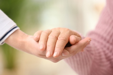 Nurse holding hand of elderly woman against blurred background, closeup. Assisting senior generation