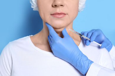Mature woman with double chin receiving injection on blue background, closeup