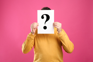 Man holding paper with question mark on pink background