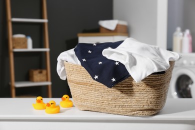 Photo of Laundry basket with baby clothes and rubber ducks on table in bathroom