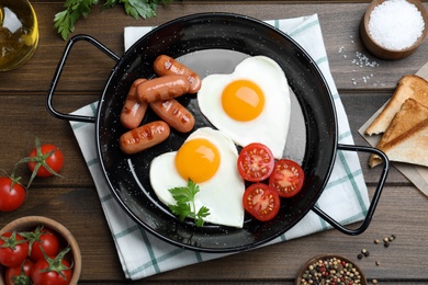 Romantic breakfast with fried sausages and heart shaped eggs on wooden table, flat lay. Valentine's day celebration
