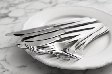 Plate with knives and forks on white marble table, closeup