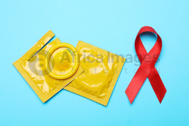Yellow condoms and red ribbon on light blue background, flat lay. LGBT concept