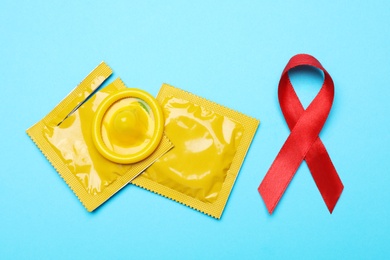 Yellow condoms and red ribbon on light blue background, flat lay. LGBT concept