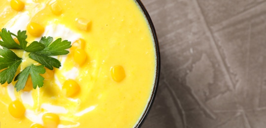 Delicious creamy corn soup served on grey table, top view