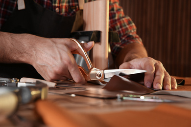 Man cutting leather with scissors at table, closeup