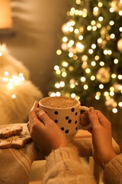 Photo of Woman with cup of hot drink and Christmas cookies at home, closeup