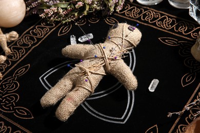 Voodoo doll pierced with pins surrounded by ceremonial items on table. Curse ceremony