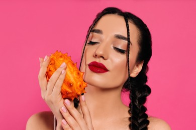 Photo of Young woman with fresh kiwano on pink background. Exotic fruit