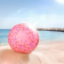 Pink beach ball on sandy coast near sea