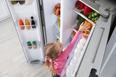 Little girl near open refrigerator indoors, above view