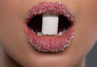 Photo of Woman with beautiful lips eating sugar cube on grey background, closeup