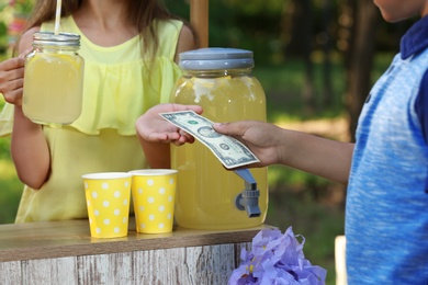 Little girl selling natural lemonade to African-American boy in park, closeup. Summer refreshing drink