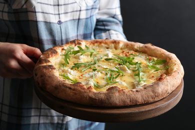 Photo of Woman holding delicious cheese pizza with arugula on black background, closeup