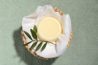 Solid shampoo bar in wicker basket on pale green fabric, top view