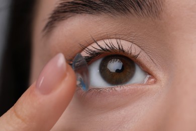 Closeup view of young woman putting in contact lens