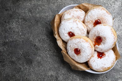Delicious donuts with jelly and powdered sugar in bowl on grey table, top view. Space for text