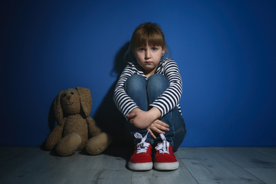 Photo of Abused little girl with toy near blue wall. Domestic violence concept