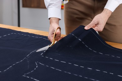 Tailor cutting fabric by following chalked sewing pattern at table in workshop, closeup