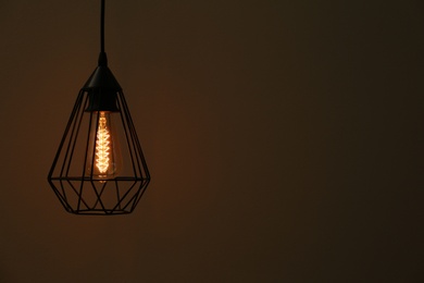 Photo of Hanging lamp bulb in chandelier against dark background, space for text