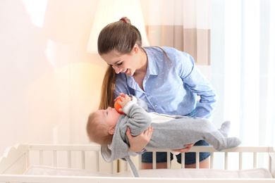 Teen nanny putting cute little baby in crib at home. Daytime sleep