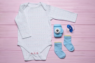 Photo of Baby clothes and camera on pink wooden background, flat lay