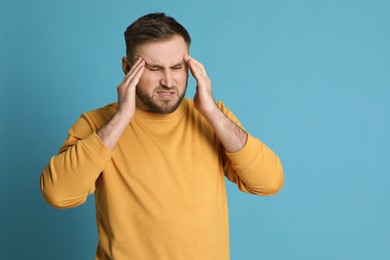 Man suffering from migraine on light blue background, space for text