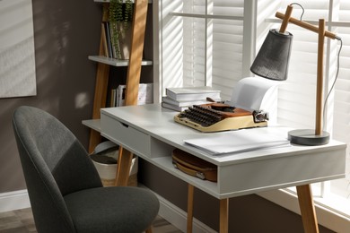Comfortable writer's workplace interior with typewriter on desk in front of window