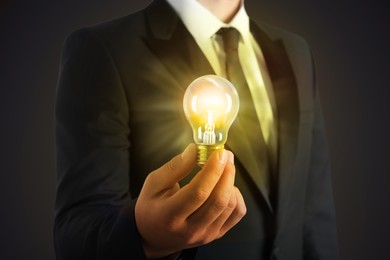 Glow up your ideas. Businessman holding light bulb on dark background, closeup
