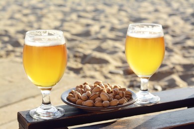 Glasses of cold beer and pistachios on wooden table outdoors