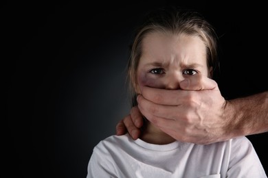 Man covering scared little girl's mouth on black background, space for text. Domestic violence