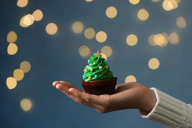 Woman holding tasty Christmas cupcake against blurred festive lights, closeup