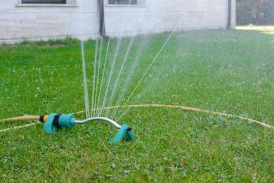 Photo of Automatic sprinkler watering green grass on lawn outdoors