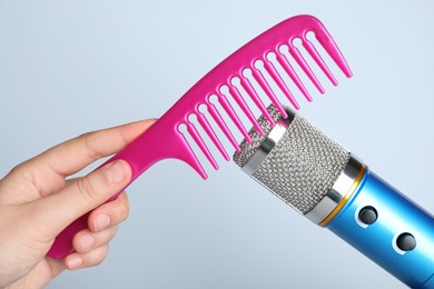 Woman making ASMR sounds with microphone and comb on grey background, closeup