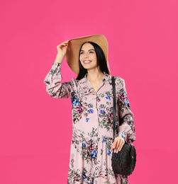 Young woman wearing floral print dress and straw hat on pink background. Space for text