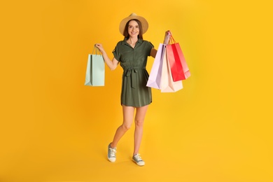 Beautiful young woman with paper shopping bags on yellow background