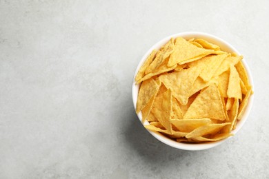 Photo of Bowl with tasty tortilla chips (nachos) on grey table, top view. Space for text