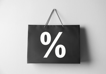 Black paper shopping bag with percent sign hanging on white wall. Discount concept