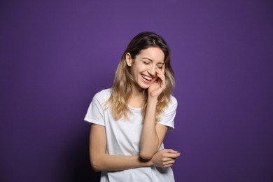 Cheerful young woman laughing on violet background