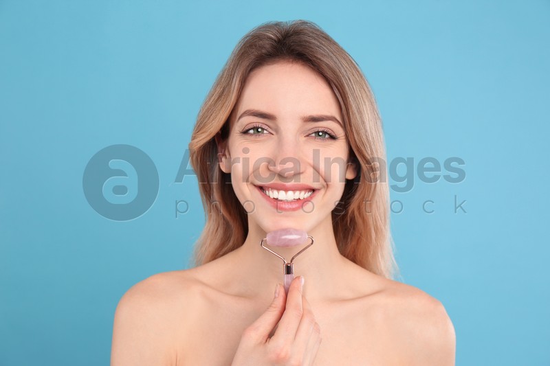 Photo of Young woman using natural rose quartz face roller on light blue background