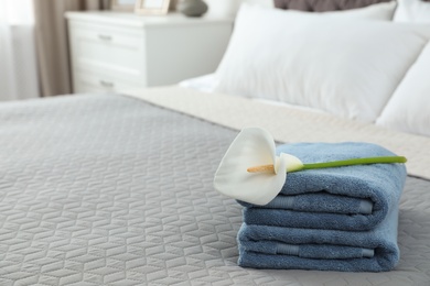 Stack of clean towels with flower on bed indoors. Space for text