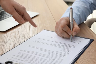 Businesspeople signing contract at wooden table, closeup